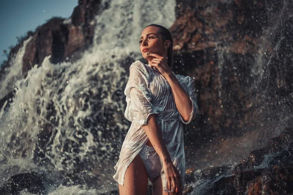 Jeune femme en chemise blanche et bikini se tient près de la cascade . — Photo