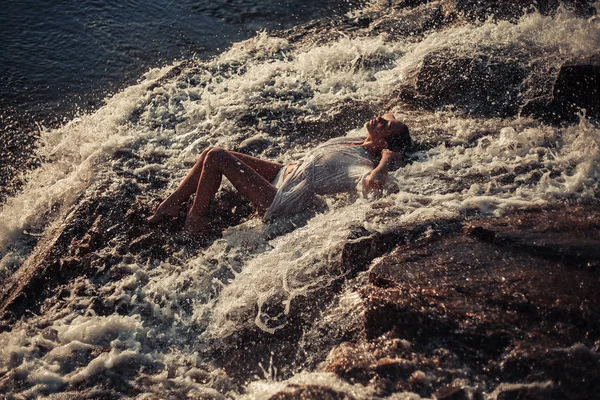 Jonge vrouw in wit shirt en bikini ligt op rots in waterstroom — Stockfoto