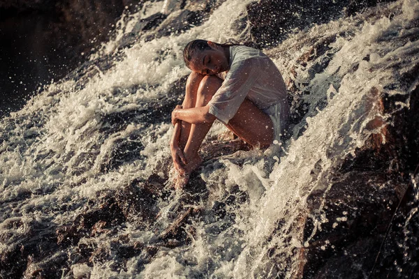 Jonge vrouw in wit shirt en bikini zit op rots in waterstroom — Stockfoto