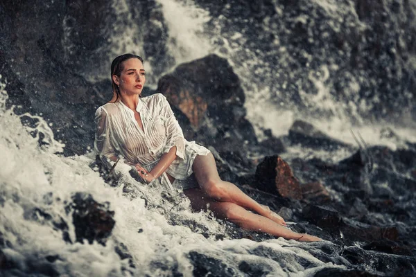 Jeune femme en chemise blanche et bikini repose sur la roche dans l'écoulement de l'eau — Photo
