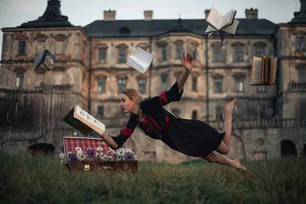 Woman sorceress reads book and flies in air against backdrop of ancient castle. Levitation. — Stock Photo, Image