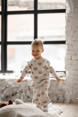 Yürümeye başlayan çocuk pijama pencere ve gülüyor yanında duruyor.