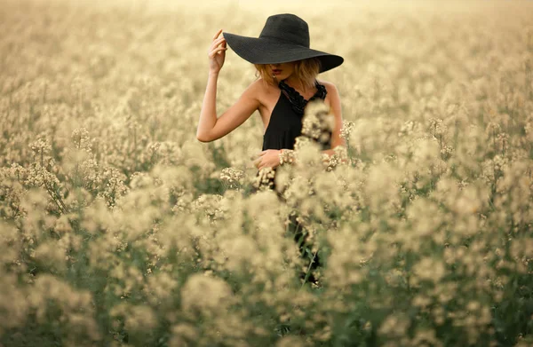 Siyah elbise ve şapka çiçekli çayır arasında genç kadın. — Stok fotoğraf