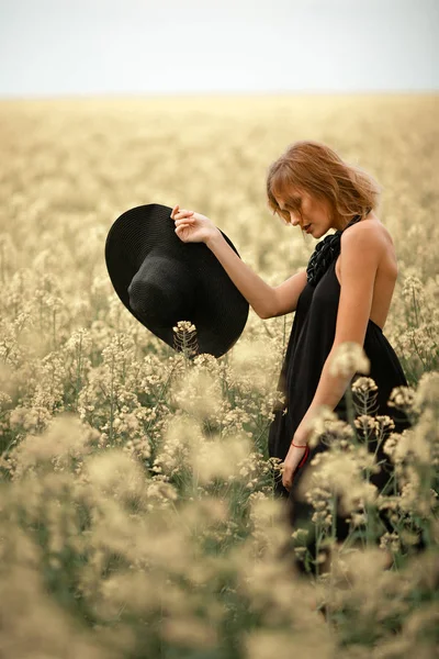 Молода жінка в чорній сукні і капелюсі в руці серед квітучих м — стокове фото
