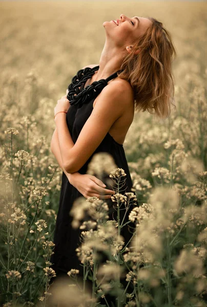 Jovem feliz em vestido preto entre o prado florido . — Fotografia de Stock