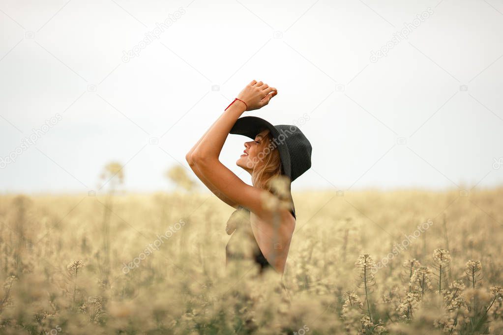 Young woman in black dress and hat among flowering meadow.