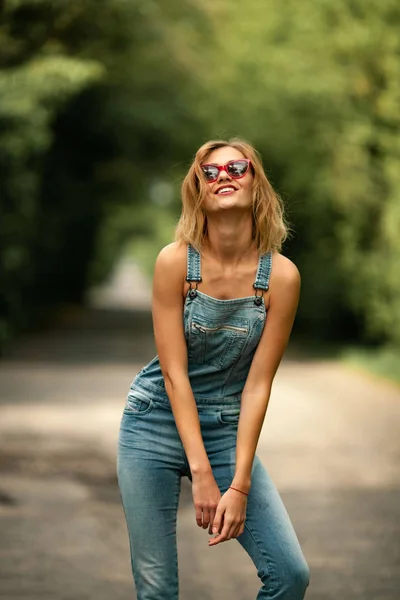 Young woman in denim overalls on forest road. — Stock Photo, Image