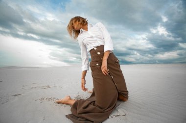 Üzgün kadın çölde gökyüzü arka plan üzerinde diz çökmüş.