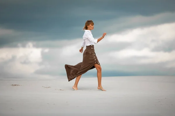 Jonge vrouw gaat barefoot in woestijn op hemelachtergrond. Zijaanzicht — Stockfoto
