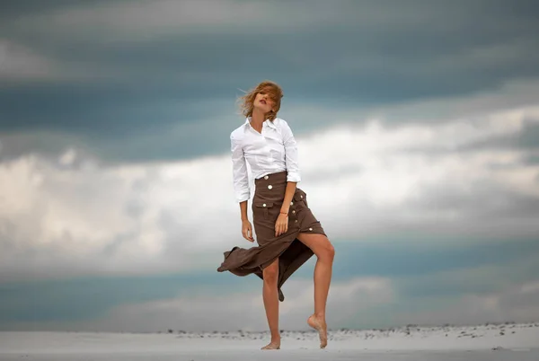 Jonge vrouw staat in de woestijn op de hemelachtergrond barefoot. — Stockfoto