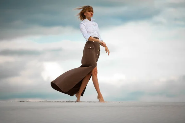 Young woman goes barefoot in desert on sky background. Side view — Stock Photo, Image