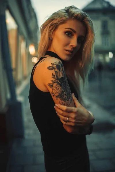 Portret młodej kobiety z tatuażem na ramieniu stojąc na ulicy w godzinach wieczornych. — Zdjęcie stockowe