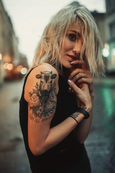 Portret młodej kobiety z tatuażem na ramieniu stojąc na ulicy w godzinach wieczornych. — Zdjęcie stockowe