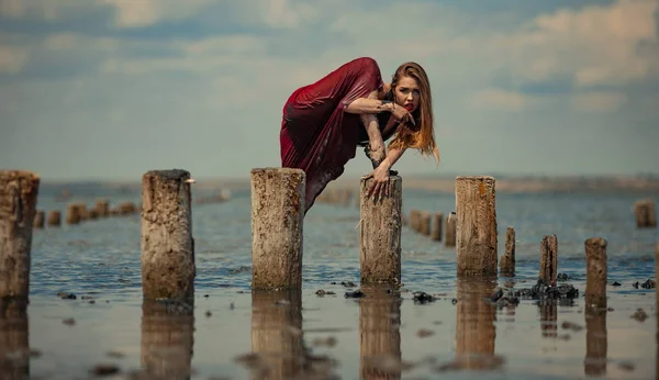 Piros ruhás fiatal nő táncol a víz tengeri háttér. — Stock Fotó
