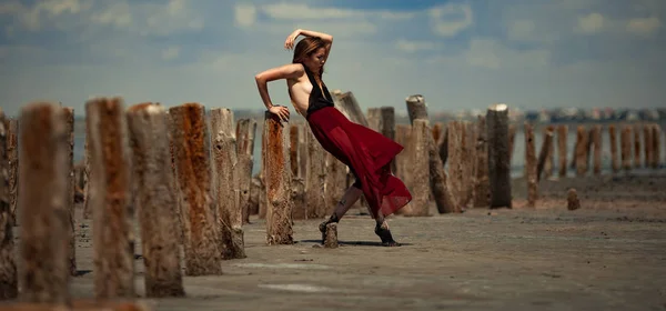Jovem mulher de vestido longo está dançando na areia no fundo da praia . — Fotografia de Stock