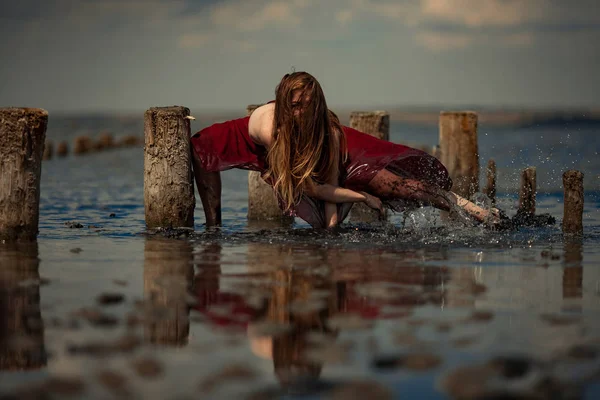 Giovane donna in abito lungo sta ballando in acqua sullo sfondo del mare . — Foto Stock