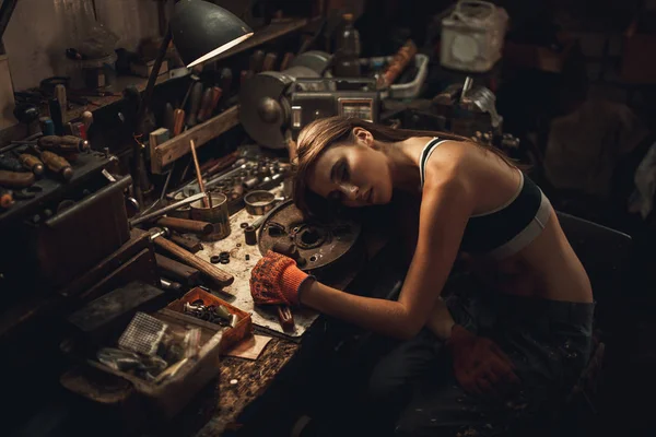 Εργαζόμενο κορίτσι σε t-shirt κάθεται στο εργαστήριο μεταξύ εργαλεία και τα υπόλοιπα στο — Φωτογραφία Αρχείου