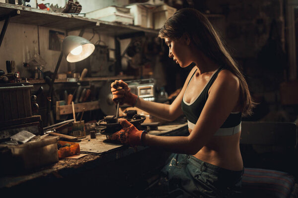 Girl worker in t-shirt sits in workshop among tools and unscrews — Stock Photo, Image