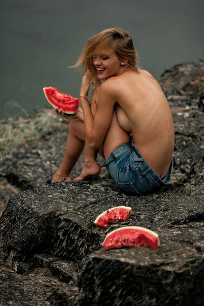 Sexy joven risueño mujer iin pantalones cortos se sienta en topless en la roca con s —  Fotos de Stock