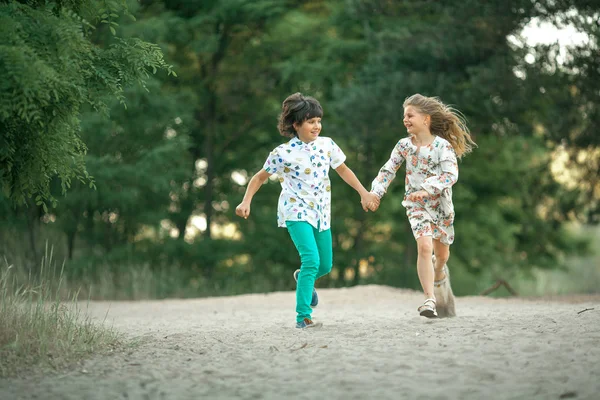 Little girl and boy are running in forest and holding hands.