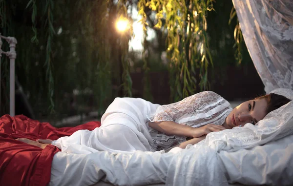 寝具、木の近くの天蓋ベッドで物思いにふける女嘘. — ストック写真