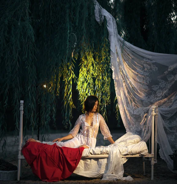 Jonge sexy vrouw ligt op bed met beddengoed en baldakijn in de buurt van boom. — Stockfoto