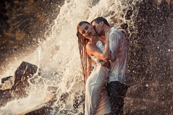 Junges verliebtes Paar umarmt und küsst sich unter Wasserfall-Gischt. — Stockfoto