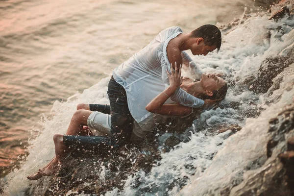 Young enamored couple lies on rock and hugs under spray of waterfall. — Stock Photo, Image