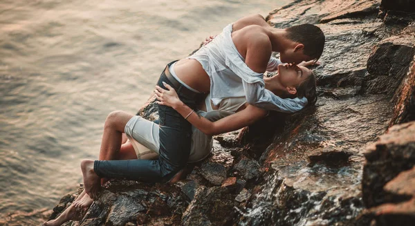 Jeune couple amoureux se trouve sur la roche, câlins et baisers sous la pulvérisation de cascade . — Photo