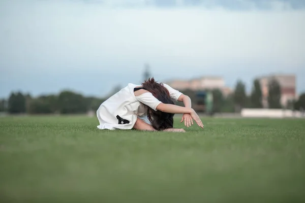 Балерина сидить на газон і зігнуті аж до її ніг. — стокове фото