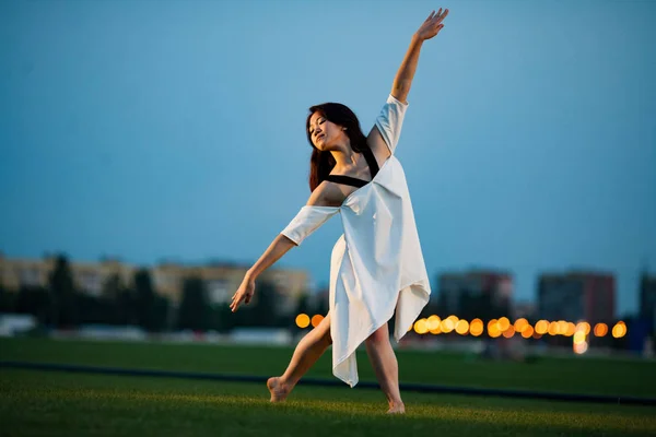 Ballerina vor dem Hintergrund von Rasen, Gebäuden und Abendlichtern. — Stockfoto