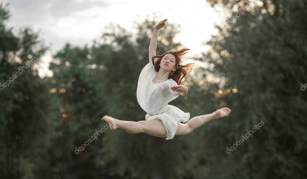 Ballerina in dress jumps on trees background.