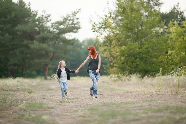 Menina feliz com sua mãe de mãos dadas e correr ao longo da estrada da floresta — Fotografia de Stock