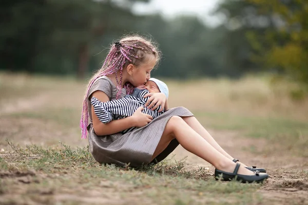 Child girl sits on grass with her newborn brother on walk in par — Stock Photo, Image