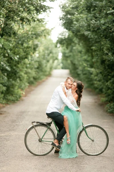 Novia y novio se sientan en bicicleta en el camino del bosque, abrazan y besan . — Foto de Stock