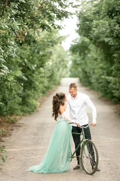 Novia y novio de pie junto a la bicicleta en la carretera forestal . — Foto de Stock