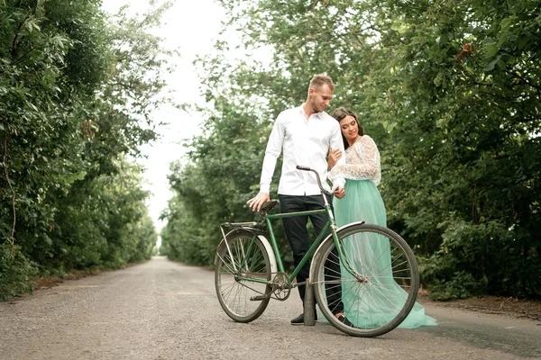 Novia y novio de pie junto a la bicicleta en la carretera forestal . — Foto de Stock