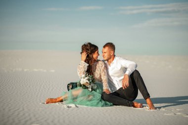 Gelin ve damat çıplak ayakla beyaz kum Çölü'nde oturup, kucakla ve lo