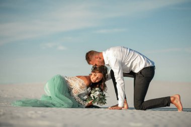 Gelin ve damat çıplak ayakla beyaz kum Çölü, sarılmak ve sm oturmak