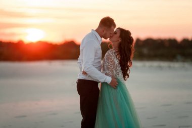 Gelin ve damat çölde günbatımı, kucak ve öpücük dur. Yan VI