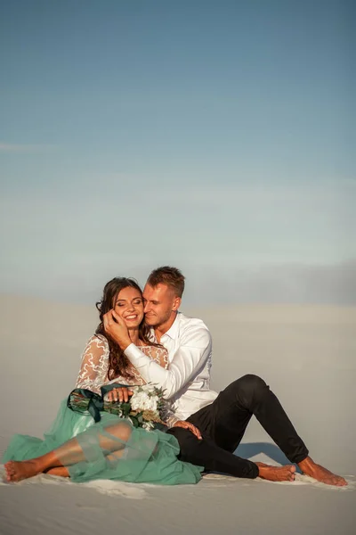 Novia y novio sentarse descalzo sobre arena blanca en el desierto, abrazo y sm — Foto de Stock