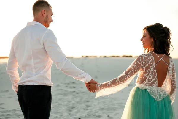 La novia y el novio van a la arena en el desierto, se toman de la mano y miran a cada uno — Foto de Stock