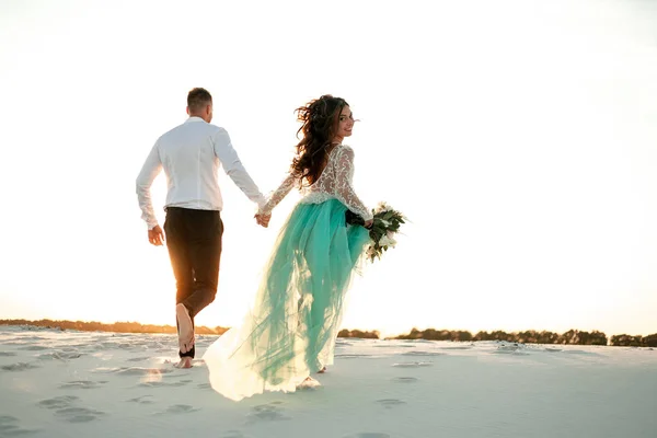 La novia y el novio corren sobre la arena en el desierto y la novia mira hacia atrás. Atrás — Foto de Stock