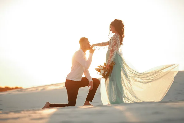 Groom fica descalço antes da noiva em um joelho no deserto em sóis — Fotografia de Stock