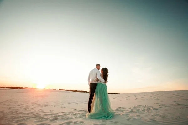 Bruden och brudgummen står på sand i öknen vid solnedgången och omfamning. B — Stockfoto