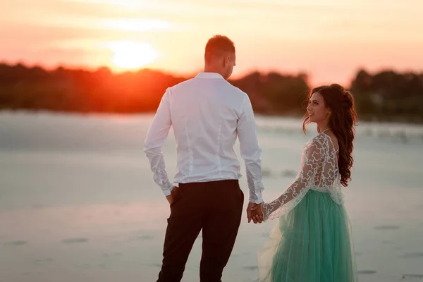 Braut und Bräutigam stehen bei Sonnenuntergang in der Wüste, halten Händchen und schauen ein — Stockfoto
