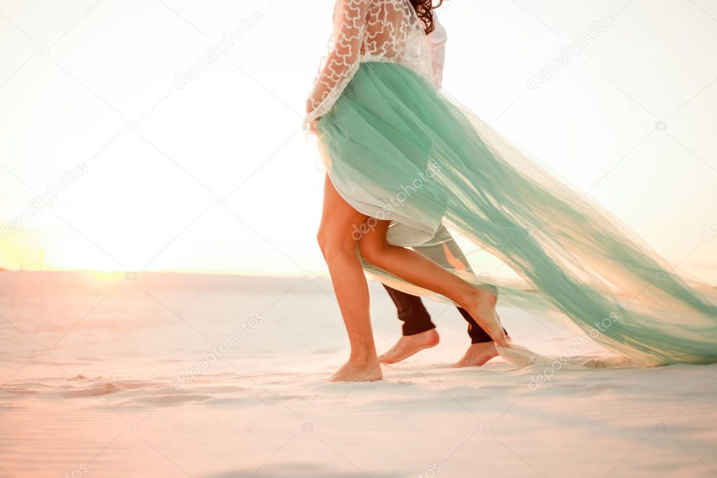 Legs of bride and groom walking barefoot in desert at sunset. Cl