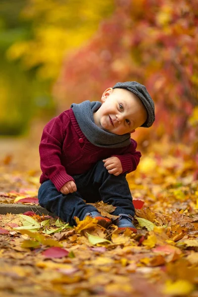 Šťastné dítě chlapeček sedí v parku na pozadí barevných au — Stock fotografie