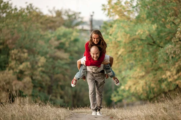 Ung man lyfte upp flicka på hans rygg och körs på skogsstigen. — Stockfoto
