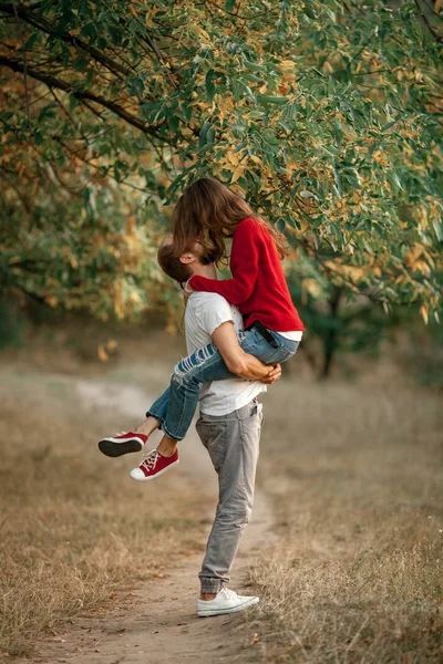 Joven hombre levantó a chica en sus manos y se besan en el paseo por el bosque . — Foto de Stock